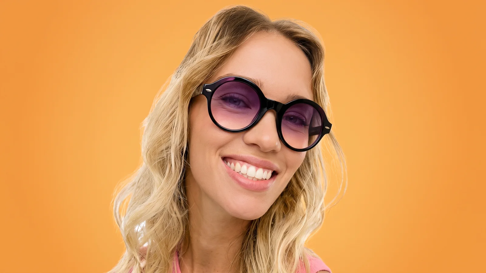 Modelo sonriente con gafas de sol redondas, sobre el naranja que recorre toda la app Magic Sunny.