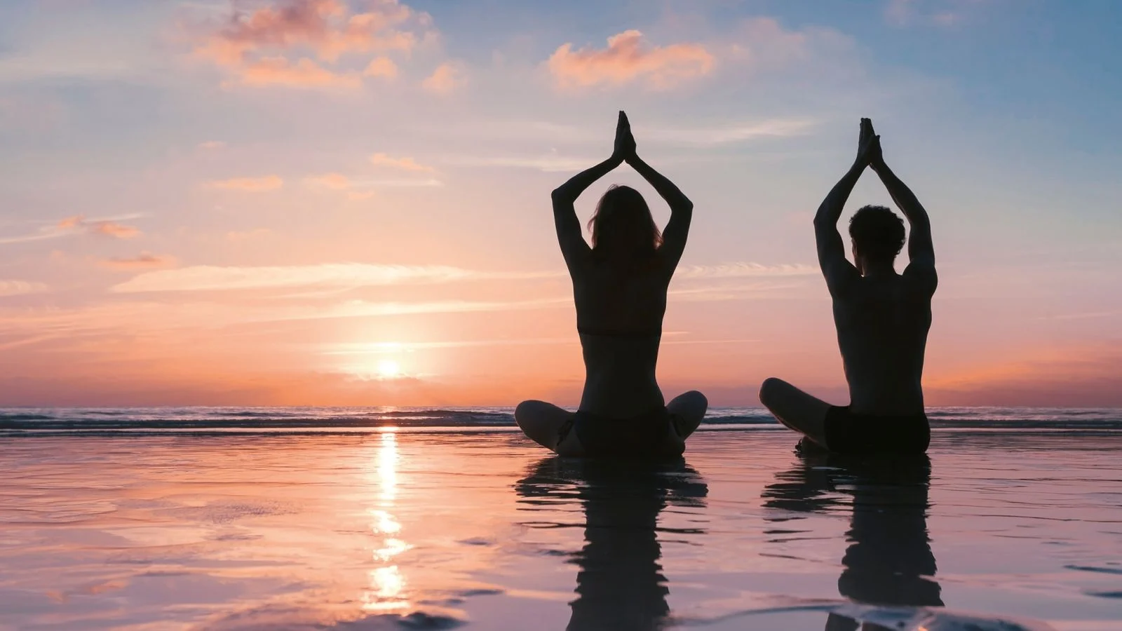 Dos personas practican yoga en la laguna al atardecer.